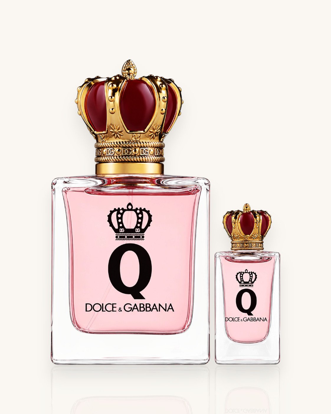 Dolce & Gabbana Q Christmas Fragrance Set, due flaconi di profumo con liquido rosa chiaro, logo Q nero e tappo a forma di corona dorata con dettagli rosso rubino, su sfondo bianco.